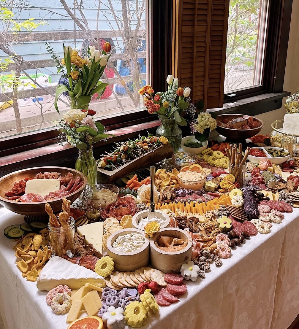Abundant grazing table with charcuterie, cheeses and spring florals by a sunlit window
